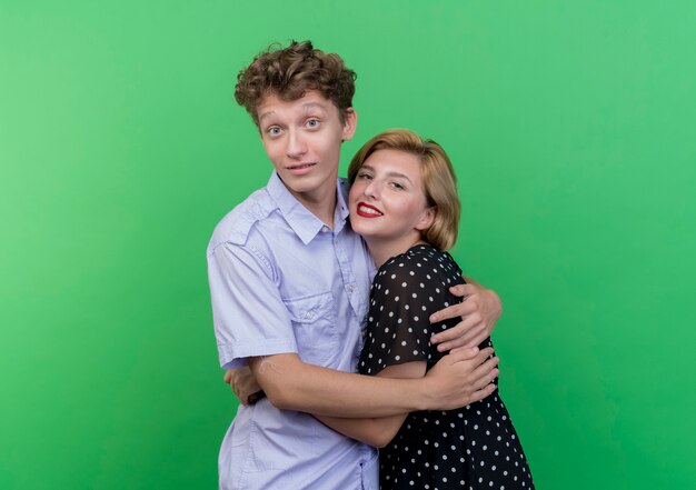 Hermosa joven pareja hombre y mujer de pie juntos hapy enamorado abrazándose de pie sobre la pared verde