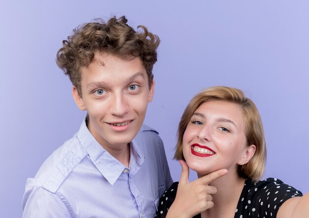 Hermosa joven pareja hombre y mujer sonriendo alegremente de pie sobre la pared azul