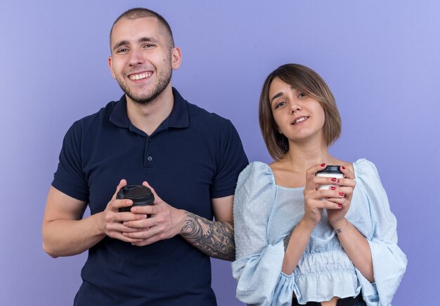 Hermosa joven pareja hombre y mujer con vasos de papel mirando sonriendo alegremente feliz y positivo de pie