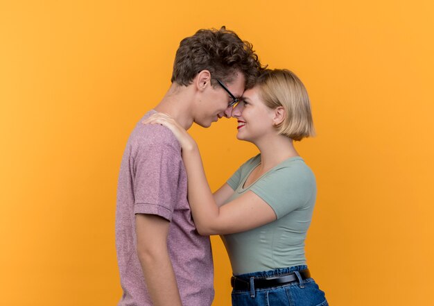 Hermosa joven pareja hombre y mujer vistiendo ropa casual de pie juntos felices enamorados abrazándose sobre la pared naranja