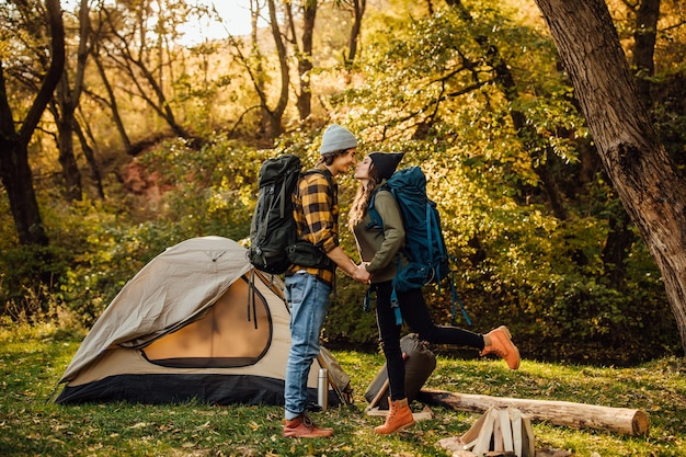 Hermosa joven pareja con mochila de senderismo besándose en el bosque cerca de la tienda