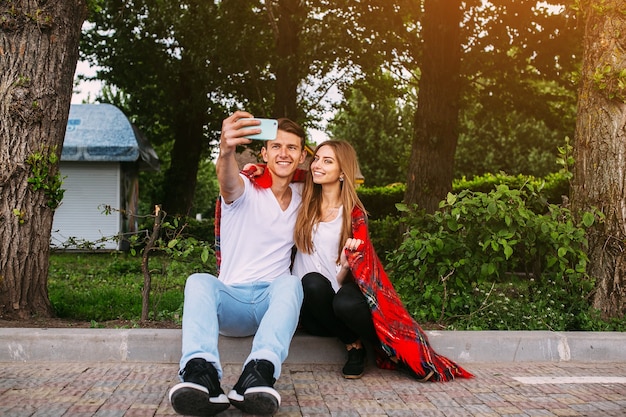 Hermosa joven pareja relajándose en el parque y hace selfie