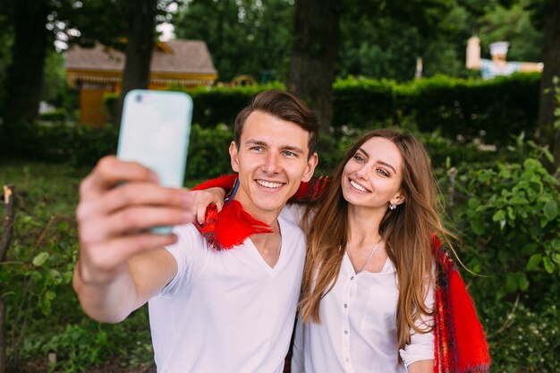 Hermosa joven pareja relajándose en el parque y hace selfie