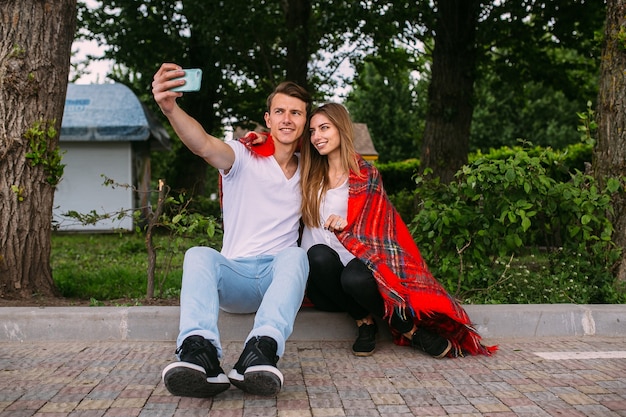 Hermosa joven pareja relajándose en el parque y hace selfie