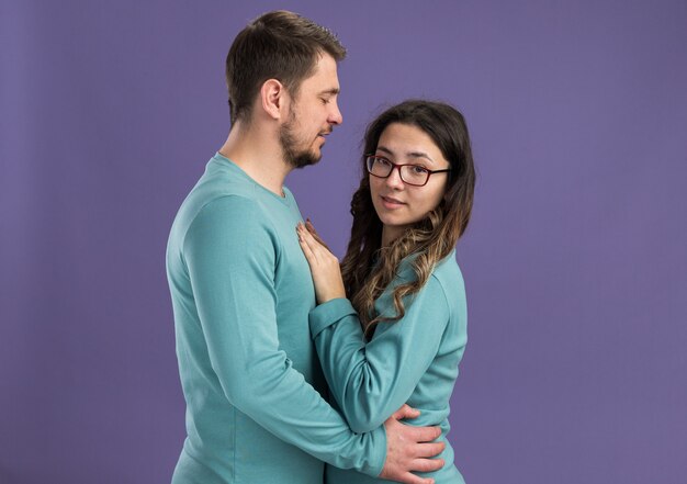 Hermosa joven pareja en ropa casual azul feliz y alegre hombre y mujer abrazando feliz en el amor celebrando el día de San Valentín de pie sobre la pared púrpura