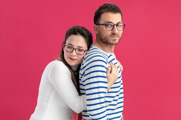 Hermosa joven pareja en ropa casual mujer feliz abrazando a su novio sonriente feliz enamorado juntos celebrando el día de San Valentín de pie sobre fondo rosa