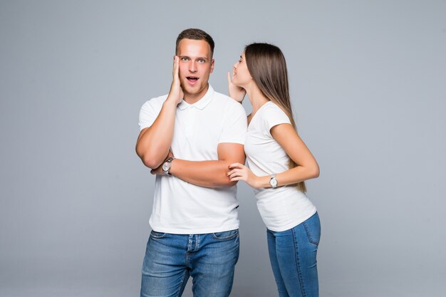 Hermosa joven pareja sorprendida en camisetas blancas y jeans con conversación secreta