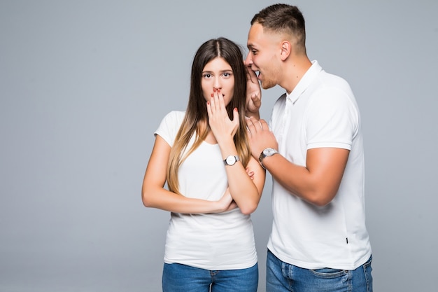 Hermosa joven pareja sorprendida en camisetas blancas y jeans con conversación secreta