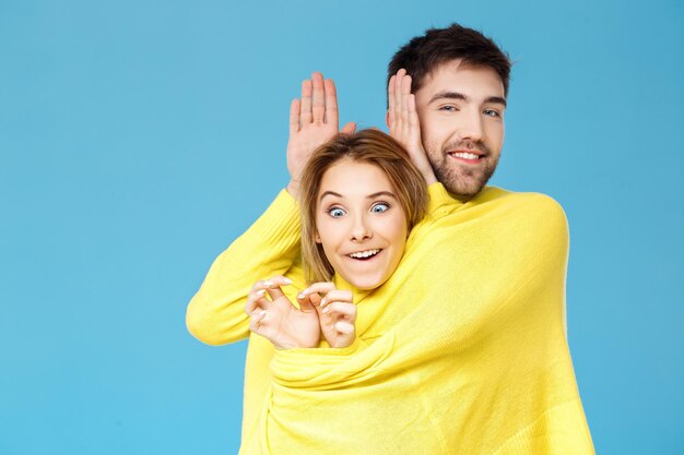 Hermosa joven pareja en un suéter amarillo posando sonriendo divirtiéndose sobre fondo azul.