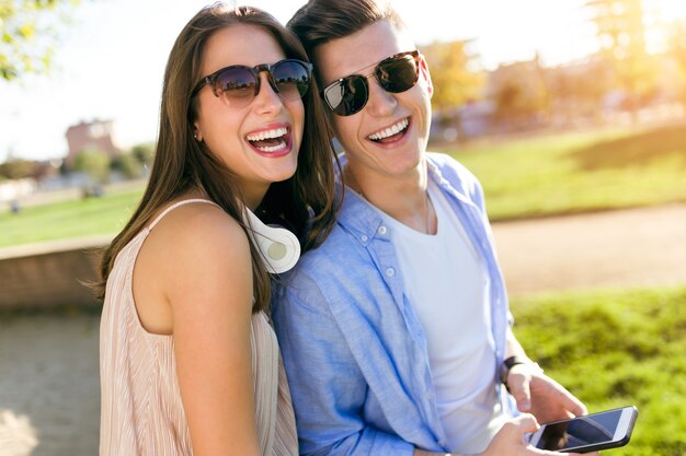 Hermosa joven pareja usando ellos teléfono móvil en el parque.