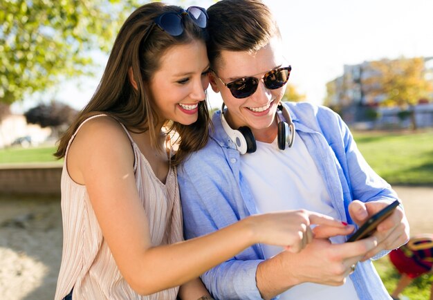 Hermosa joven pareja usando ellos teléfono móvil en el parque.