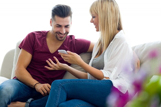 Hermosa joven pareja utilizando el teléfono móvil en casa.