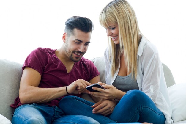 Hermosa joven pareja utilizando el teléfono móvil en casa.