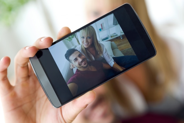 Hermosa joven pareja utilizando el teléfono móvil en casa.