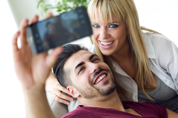 Hermosa joven pareja utilizando el teléfono móvil en casa.