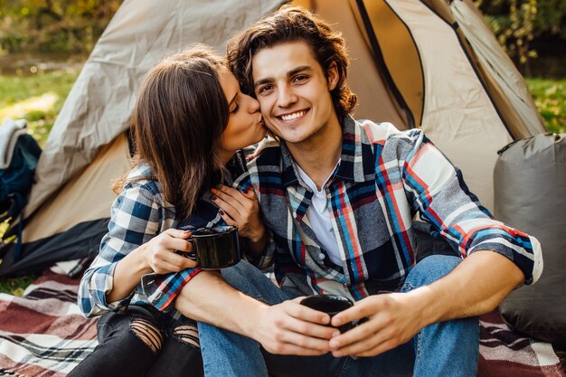 Hermosa joven pareja en vestido casual sentado en un campamento cerca de la tienda