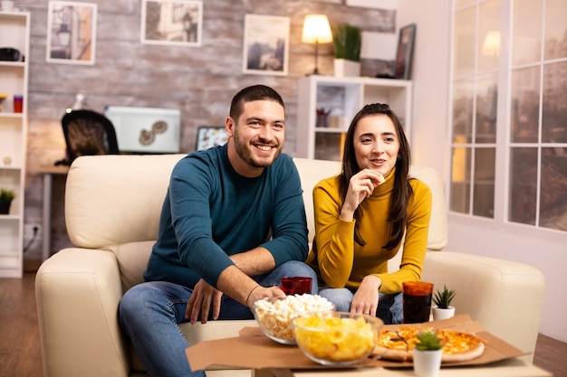 Hermosa joven pareja viendo la televisión y comiendo comida rápida para llevar en la sala de estar