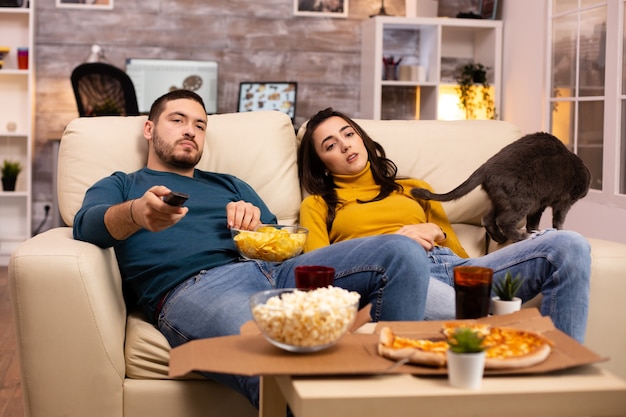 Hermosa joven pareja viendo la televisión y comiendo comida rápida para llevar en la sala de estar