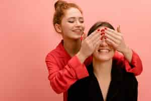 Foto gratuita hermosa joven pelirroja caucásica en camisa cierra los ojos a la hermana de pie detrás de fondo rosa estilo de vida diferentes emociones concepto de ocio