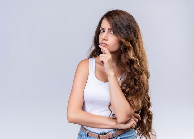 Hermosa joven pensativa poniendo el dedo en la barbilla en la pared blanca aislada con espacio de copia