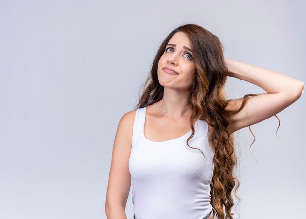 Hermosa joven pensativa poniendo la mano detrás de la cabeza y mirando hacia arriba en la pared blanca aislada con espacio de copia