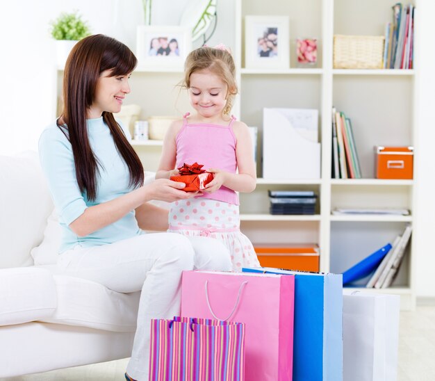 Hermosa joven y pequeña hija con regalo después de hacer compras en casa