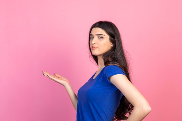 Hermosa joven de pie sobre fondo rosa y sosteniendo su mano abierta