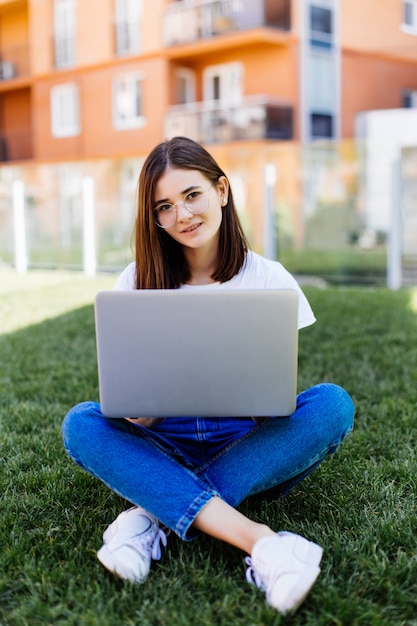 Hermosa joven con portátil sentado al aire libre en el césped