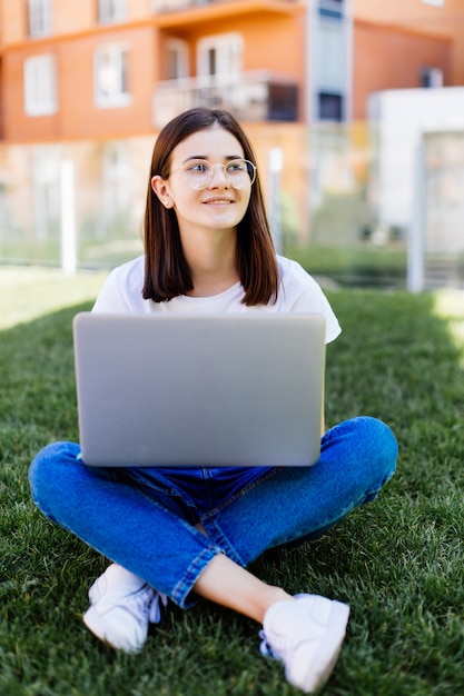 Foto gratuita hermosa joven con portátil sentado al aire libre en el césped