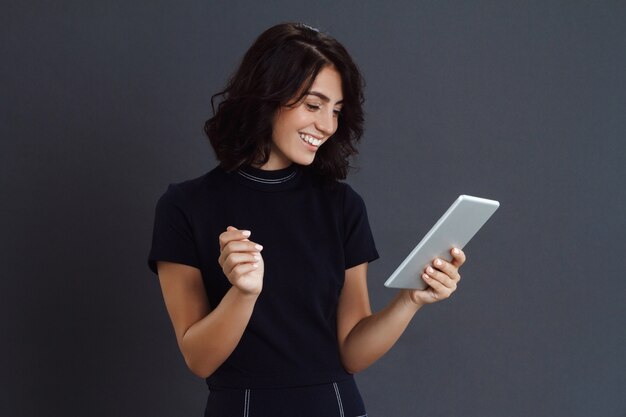 Hermosa joven posando sobre pared gris y sosteniendo la tableta en manos