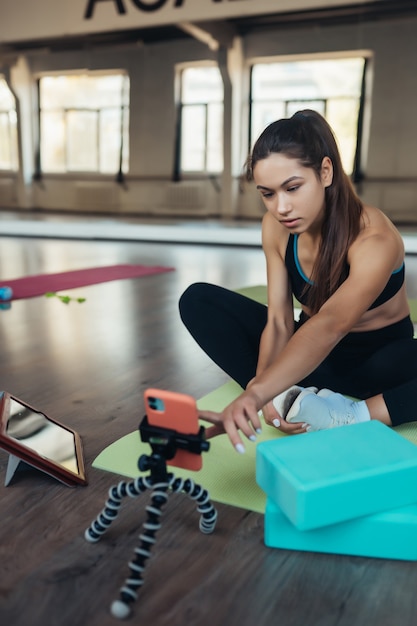 Hermosa joven practicando yoga, se compromete con el profesor en línea a través de una tableta. Concepto de deportes en casa.