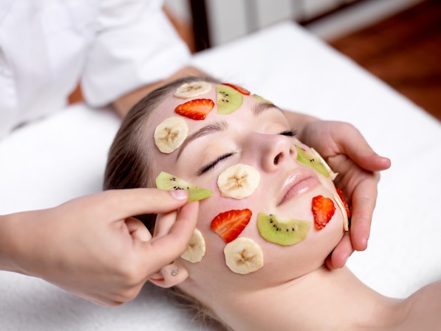 Hermosa joven recibiendo máscara de frutas en una cara en un salón de belleza