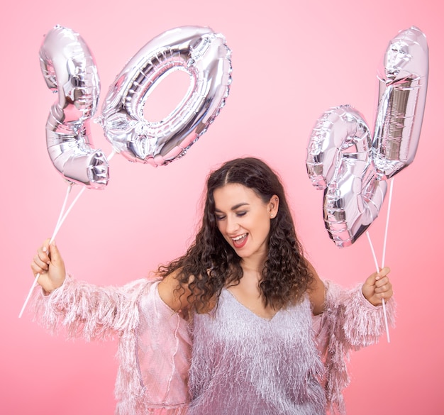 Foto gratuita hermosa joven se regocija en el año nuevo sobre un fondo rosa con globos plateados para el concepto de año nuevo