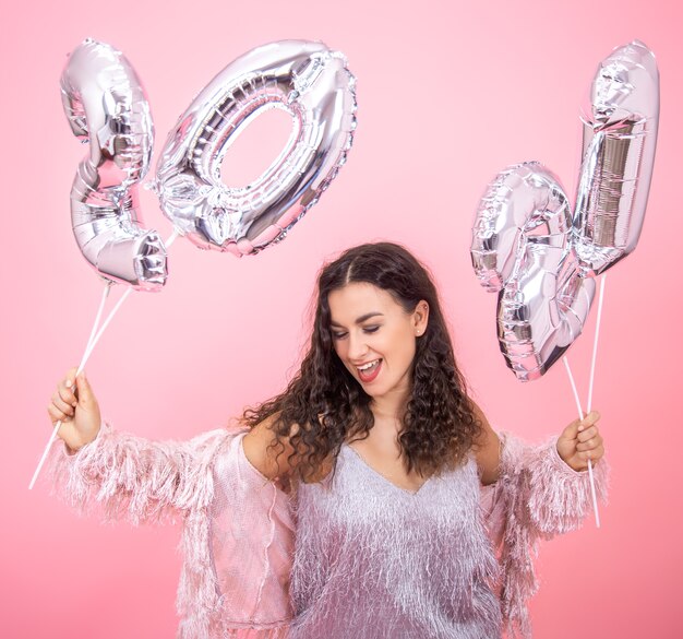 Hermosa joven se regocija en el año nuevo sobre un fondo rosa con globos plateados para el concepto de año nuevo