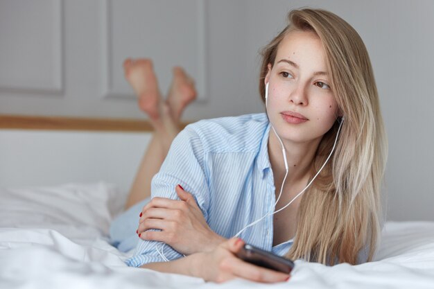 Hermosa joven relajándose en la cama y escuchando música