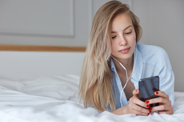 Hermosa joven relajándose en la cama y escuchando música