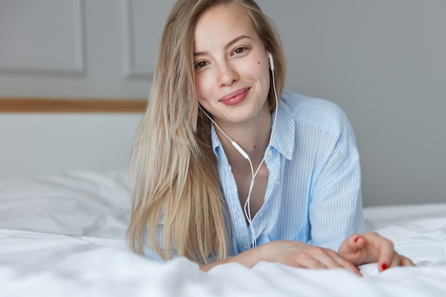 Hermosa joven relajándose en la cama y escuchando música