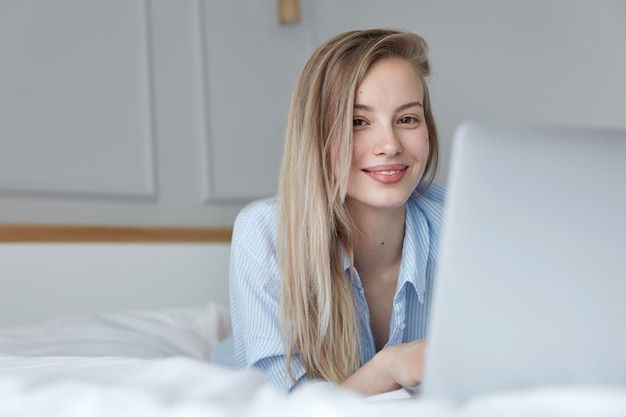 Hermosa joven relajante en la cama con un portátil