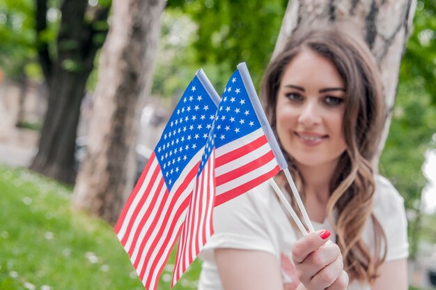 Hermosa joven rizada en ropa casual posando y sonriente, de pie con la bandera americana. Día de la independencia, celebración, concepto de patriotismo