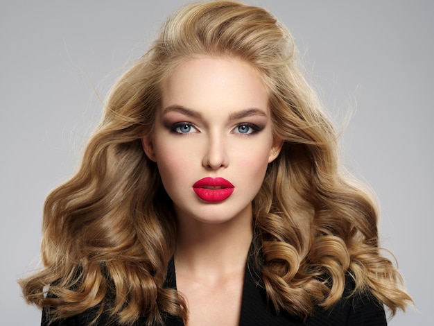 Hermosa joven rubia con labios rojos sexy. Closeup atractivo rostro sensual de mujer blanca con pelo largo. Maquillaje de ojos ahumados