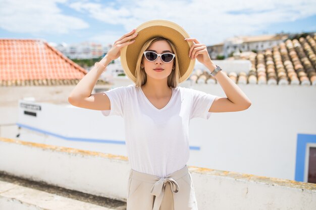 Hermosa joven rubia con sombrero y gafas de sol caminando por la calle