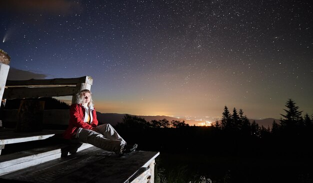 Hermosa joven sentada bajo el cielo estrellado de la noche
