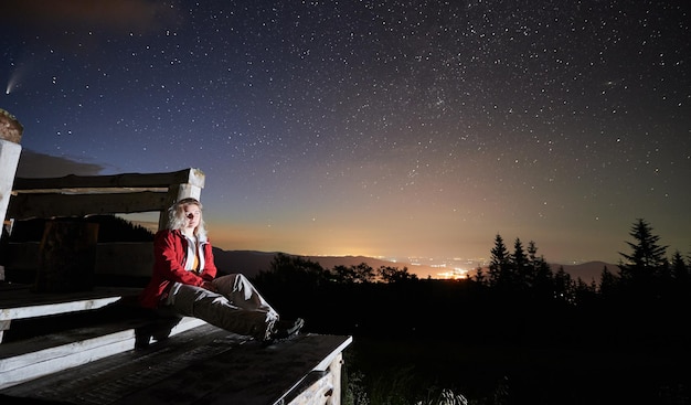 Hermosa joven sentada bajo el cielo estrellado de la noche