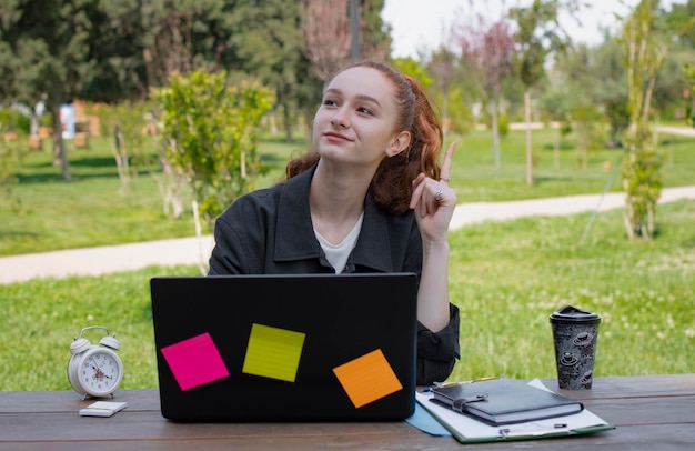 Hermosa joven sentada a la mesa en el parque usando una laptop