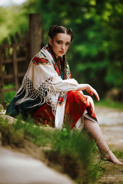 Hermosa joven se sienta en un parque con un colorido vestido ucraniano