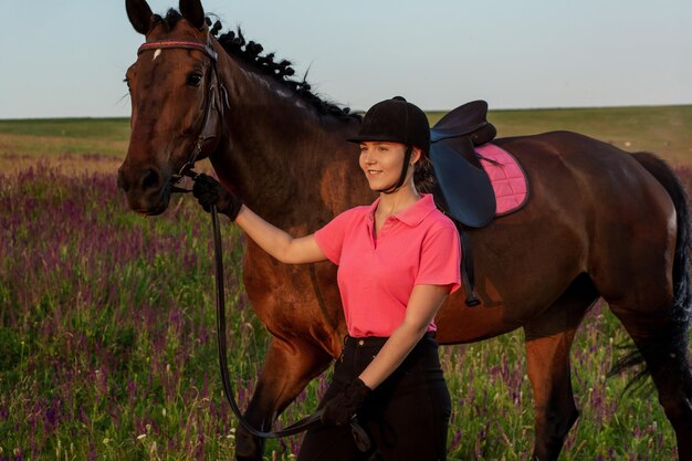 Hermosa joven sonríe a su caballo competencia uniforme de vestir: retrato al aire libre en la puesta de sol