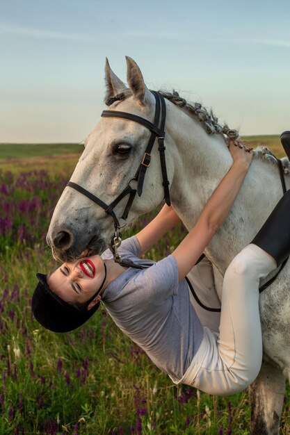 Hermosa joven sonríe a su caballo vistiendo uniforme competencia: retrato al aire libre en la puesta del sol. Cuidar de los animales, el concepto de amor y amistad.