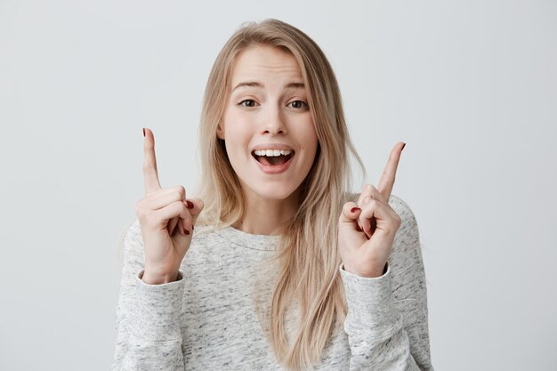 Hermosa joven sonriendo indicando algo en la pared en blanco con las manos