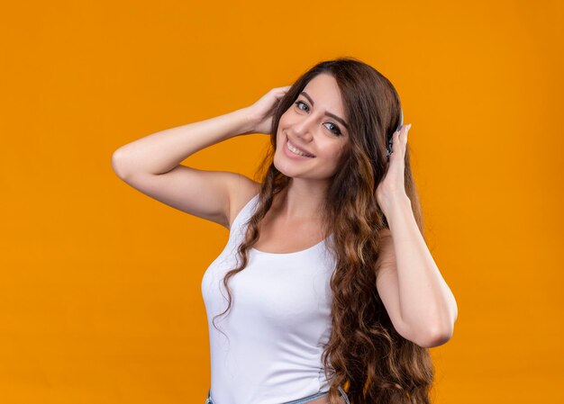 Hermosa joven sonriente con auriculares poniendo las manos sobre ellos en el espacio naranja aislado