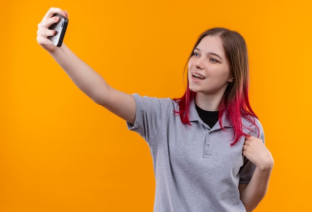 Hermosa joven sonriente con camiseta gris tomando selfie sobre fondo amarillo aislado